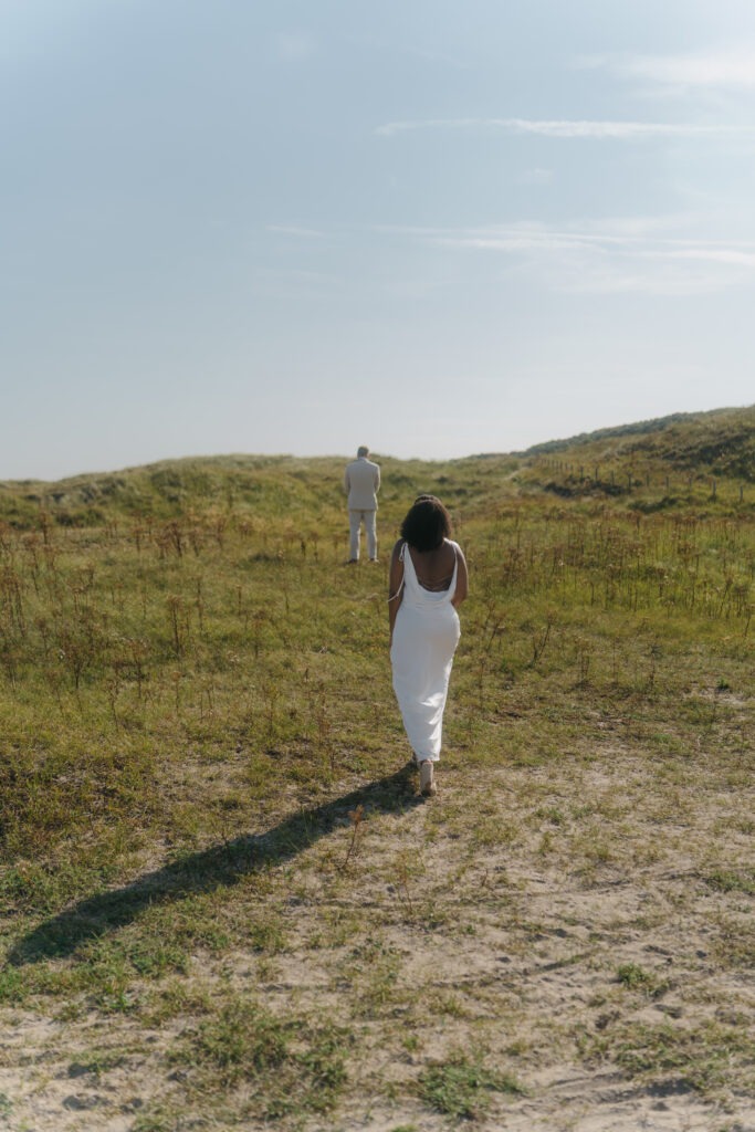 Braut nähert sich ihrem Partner in den Dünen zum First-Look – emotionale Elopement Fotografie